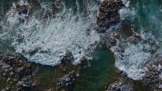 Strong waves crash spreading whitewash across rocky shore drone top down static FREE STOCK VIDEO [upl. by Ennoira]